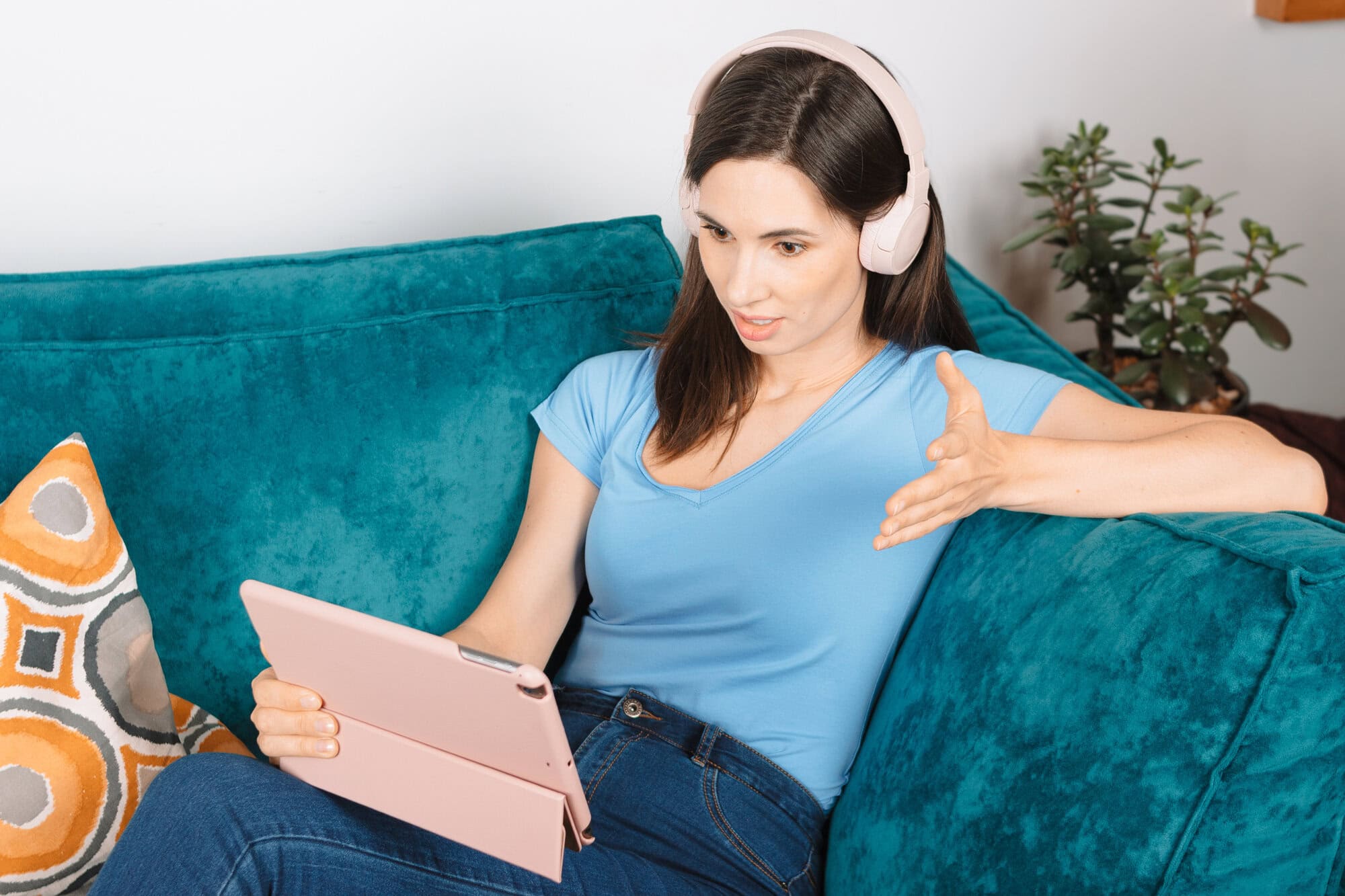 Close up view portrait young attractive millennial woman sits on couch in headphones in living room having unpleasant video call conversation using digital tablet. Brunette girl has spirited debate
